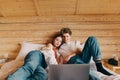 Positive young man and woman couple watching movie on laptop, lying in wooden apartment on bed. Couple relaxing watching a movie