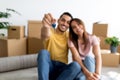 Positive young multiracial couple showing house key, sitting on floor of new home, selective focus Royalty Free Stock Photo