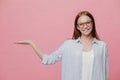 Positive young smiling woman raises hand, pretends holding something, gestures over copy space, dressed in sylish oversized shirt