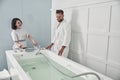 Specialist prepares hydro massage tub with clear water to mature guest in spa salon