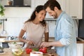 Positive young spouses cooking food enjoying pleasant conversation at kitchen