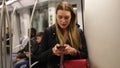 Positive young woman absorbed in her smartphone while traveling in subway car