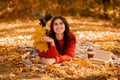 Positive young woman in cozy sweater lying on picnic blanket outdoors with fall leaves, book and takeout coffee Royalty Free Stock Photo