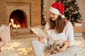 Positive young woman enjoying to spend time with her dog, adorable female posing in festive living room with her pet, reading book Royalty Free Stock Photo