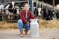 Positive young woman farmer squatting at milk can