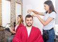 Positive young woman hairdresser cuts hair of young man client Royalty Free Stock Photo