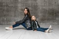 Positive young woman and little girl in similar rock style clothing jeans and black leather jackets sitting back to back