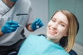 Positive young woman sit in chairin dentistry and smile to camera. She show beautiful smile. Doctor hold tools for teeth