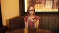 Positive young woman texting message on modern smartphone in the cafe