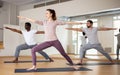 Woman standing in lunging asana Virabhadrasana in yoga studio