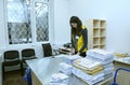 At the post office, sorting room: female postal worker in uniform sorting letters and parcels standing at the work table