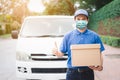 Postal delivery courier man thumbs up wearing protective face mask in front of cargo van delivering package holding box due to Royalty Free Stock Photo