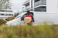 Postal delivery process. Silhouette of tall, well-build Black courier man in red jacket standing with a cardboard parcel