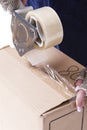 Postal and Moving. Closeup of Female Hands Packing Cardboard Box Indoors Unsing A Tape-Machine Royalty Free Stock Photo