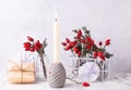 Postcard with burning candle, wrapped box with present, briar berries in bottle, against textured wall.