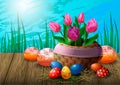 Postcard with tulips in a wicker basket, Easter eggs and cupcakes on a wooden table against the background of grass and sky