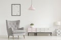 Poster above grey armchair and lamp in white living room interior with plant on cabinet. Real photo Royalty Free Stock Photo