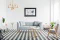 Poster above grey sofa in bright patterned living room interior with armchair and gold lamp. Real photo Royalty Free Stock Photo