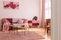 Poster above grey sofa with pillows in bright living room interior with table on pink carpet. Real photo Royalty Free Stock Photo