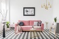 Poster above pink sofa in spacious living room interior with patterned armchair and plants. Real photo Royalty Free Stock Photo