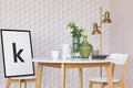 Poster in black frame on chair at wooden table with flowers in glass vase in classy dining room interior with geometric pattern on Royalty Free Stock Photo