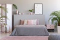 Poster on grey bedhead in bedroom interior with pink pillows on