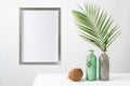 Poster mockup or silver wooden photo frame in modern style on light wall with natural palm leaves in glass vase and coconut on Royalty Free Stock Photo