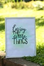 Poster with phrase Enjoy The Little Things on grass outdoors