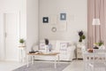 Posters above white sofa in spacious flat interior with flowers on table near door. Real photo