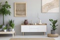 Posters on grey wall above white cupboard in living room interior with plants and pouf. Real photo Royalty Free Stock Photo