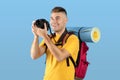Postive young guy with backpack taking picture on professional DSLR camera over blue studio background Royalty Free Stock Photo