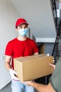 Postman, deliveryman wearing mask carry small box deliver to customer in front of door at home. Man wearing mask prevent covid19, Royalty Free Stock Photo