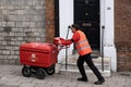 Postman employed by England\'s Royal Mail pushes a large trolley with mail