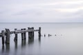 Posts of a broken pier leading out into calm blue tranquil sea w