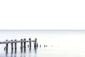 Posts of broken pier standing in a light blue lake, white sky ba