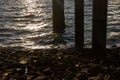 Posts under a pier and waves reflecting the sun during sunset Royalty Free Stock Photo