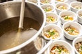 Pot of broth next to lined up bowl of chicken soup