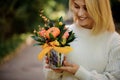 Pot with composition of flowers of green leaves in hands of young smiling woman