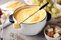 Pot of delicious cheese fondue and fork with bread on table Royalty Free Stock Photo