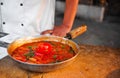 Pot filled with a steaming meal on a wooden table next to the chef