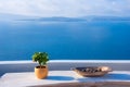 A pot with flower and a plate on a wooden table with ocean background, Santorini. Royalty Free Stock Photo