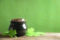 Pot of gold coins and clover leaves on wooden table against green background, space for text. St. Patrick`s Day celebration Royalty Free Stock Photo