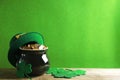 Pot of gold coins, hat and clover leaves on wooden table against green background, space for text. St. Patrick`s Day celebration Royalty Free Stock Photo