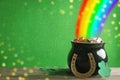 Pot with gold coins, horseshoe and clover leaves on wooden table against green background, space for text. St. Patrick`s Day Royalty Free Stock Photo