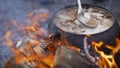 A pot of soup cooked over a fire. Stir soup with soup ladle, which is cooked in a cast iron over a fire. food in a big kettle