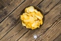 Potato chips in bowl on a wooden background, top view. Salty crisps scattered on a table Royalty Free Stock Photo