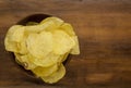 Potato chips in bowl on a wooden background, top view. Salty crisps scattered on a table Royalty Free Stock Photo