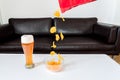 Potato chips falling out of a packet of crisps into a glass bowl with wheat beer on white couch table Royalty Free Stock Photo