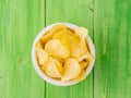 Potato chips in white bowl on wooden table bright green Royalty Free Stock Photo