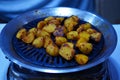 Potato cuts being roasted on a small barbeque machine on a gas stove at night.